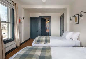 A hotel room with two beds, a window with curtains, a door, and a wall-mounted light fixture. - The Arnold House (Livingston Manor)