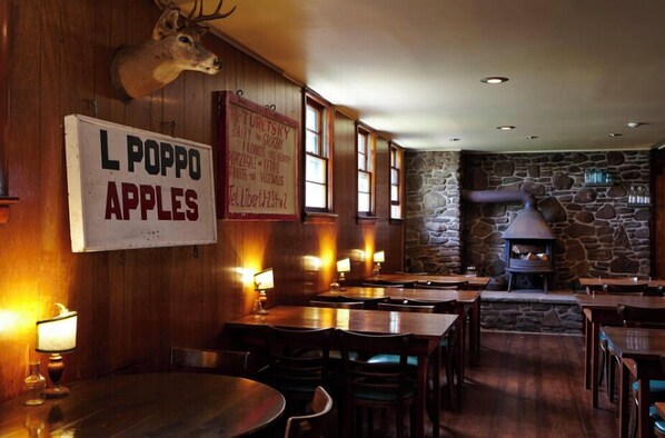 A rustic restaurant interior with wooden walls, a stone fireplace, and a sign advertising 'L POPPO APPLES'. - The Arnold House (Livingston Manor)