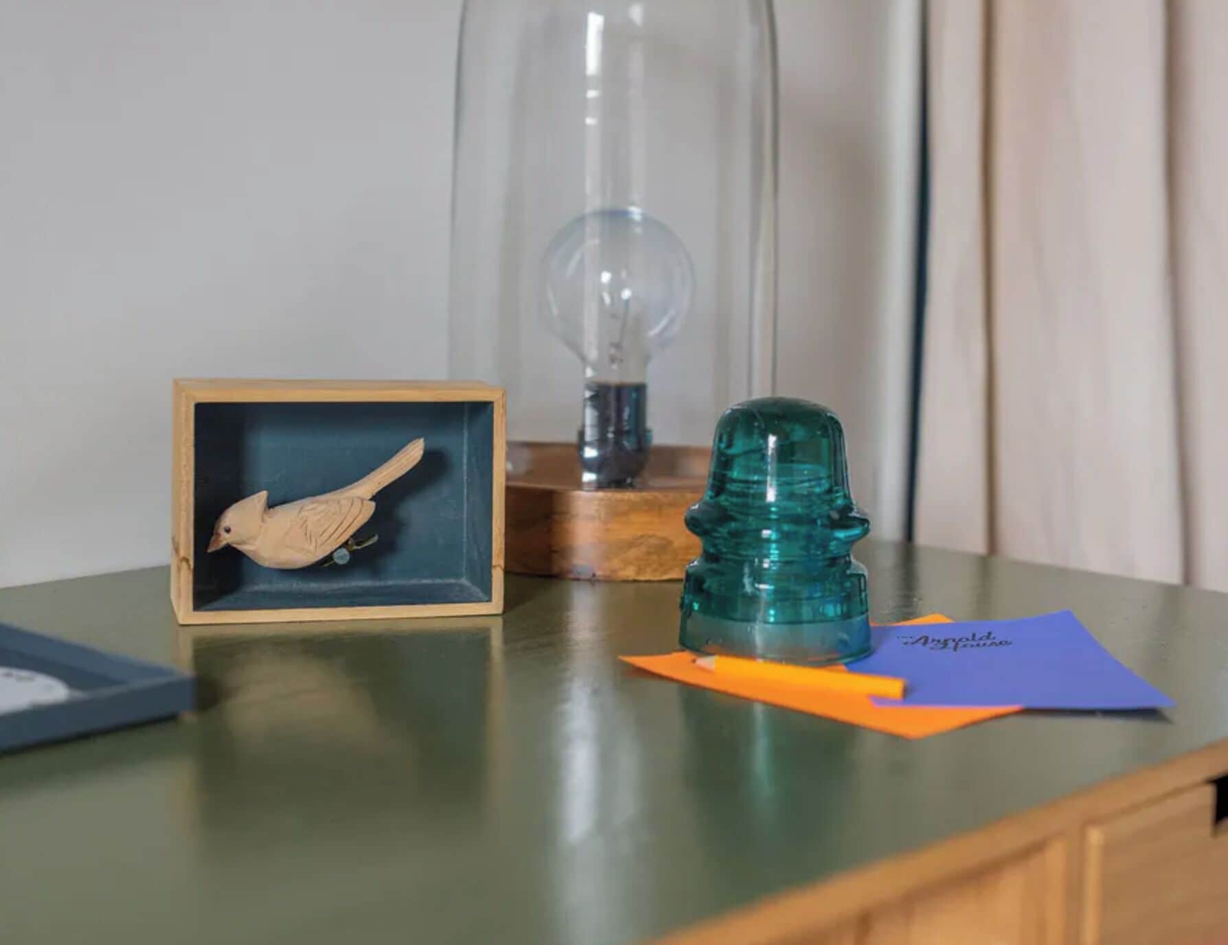 A wooden box with a bird sculpture, a green glass object, and a blue envelope on a table.