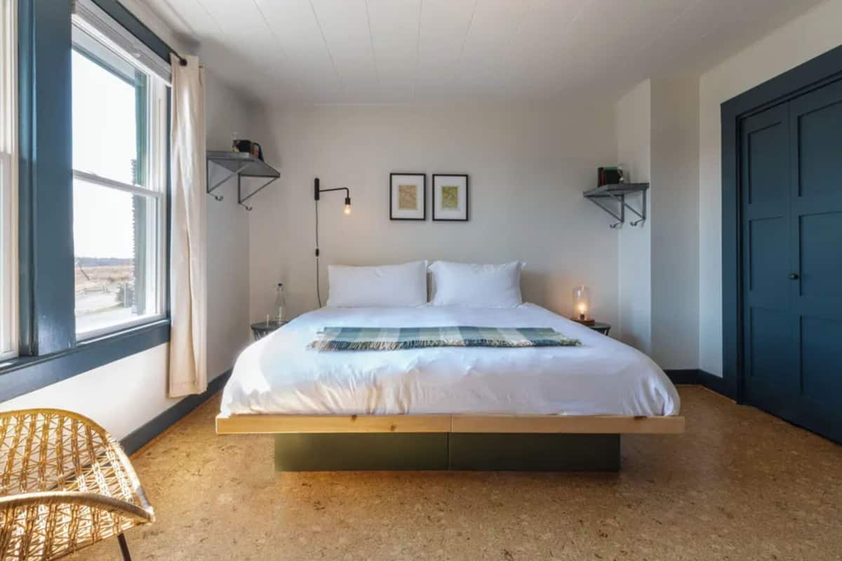 A bedroom with a large bed, a window with curtains, a chair, and a door.