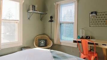 A bedroom with a bed, a desk, a chair, a window, and a shelf with books.