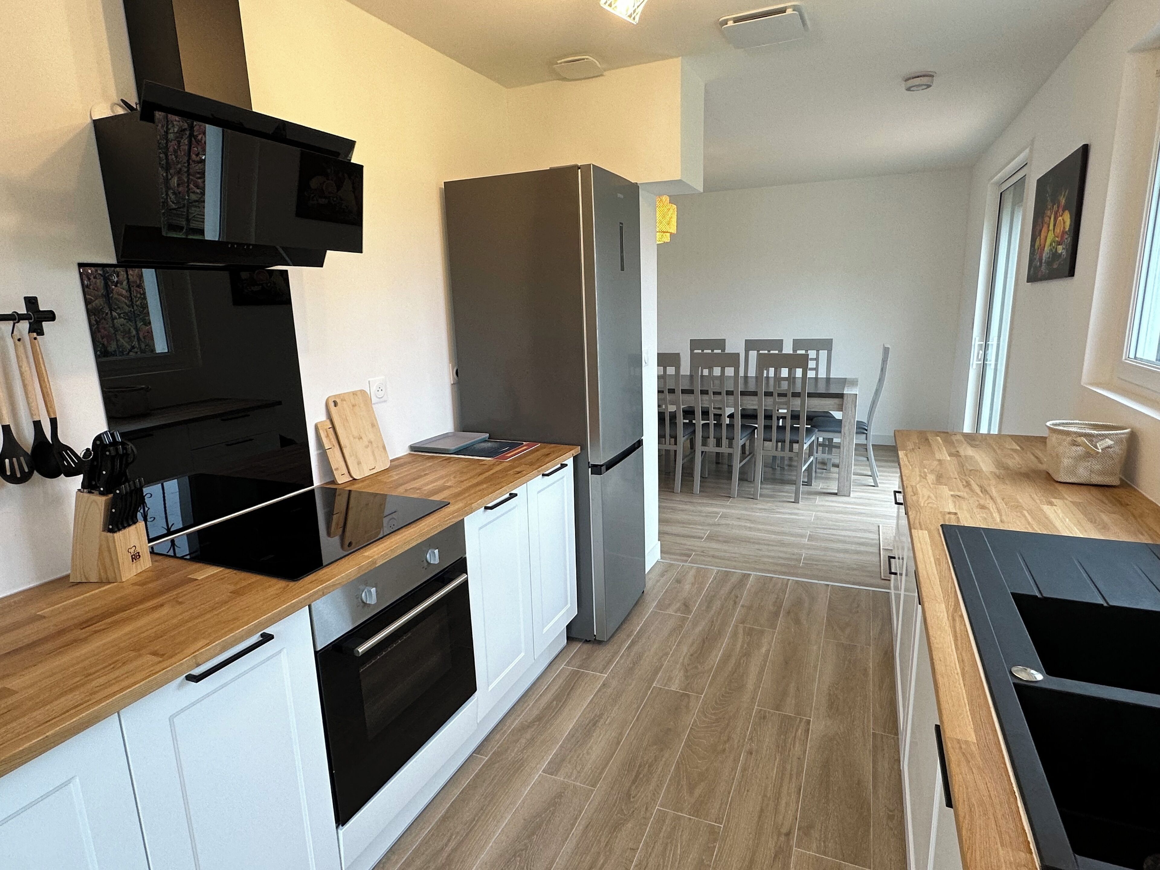 A modern kitchen with white cabinets, a stainless steel refrigerator, and a wooden countertop.