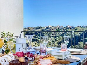 A balcony with a table set for a meal, overlooking a hillside with houses. - Sevenhouse by Atlantic Holiday (Machico)