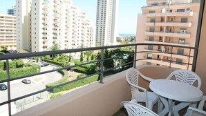 En balkon med hvide stole og et bord, udsigt over en vej og bygninger.