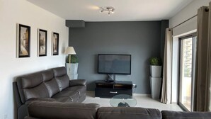 A modern living room with a dark brown leather sofa, a flat-screen TV, and framed artwork on the wall. - 3 Bedroom apartment Paraiso Sol da Rocha (Portimão)