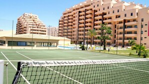 A tennis court with a net in the foreground, surrounded by multi-story residential buildings. - 3 Bedroom apartment Paraiso Sol da Rocha (Portimão)