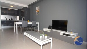 Ein modernes Wohnzimmer mit Fernseher, einem Essbereich mit Stühlen und einer Küche im Hintergrund.