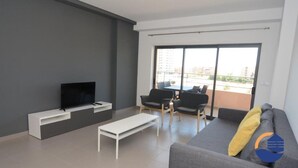 Ein modernes Wohnzimmer mit Flachbildfernseher, einer Couch, einem Couchtisch und einem Balkon mit Sitzgelegenheit im Freien.