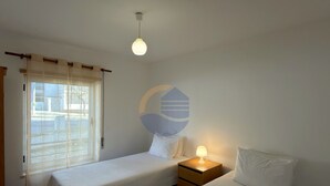 Une chambre d’hôtel avec deux lits, une table de chevet avec une lampe, une fenêtre avec des rideaux et un mur orné d’un logo.