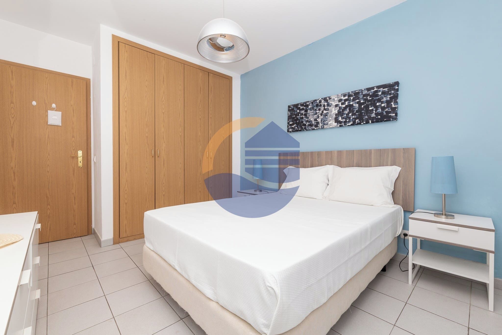 A bedroom with a bed, bedside table, lamp, and a wall-mounted artwork.