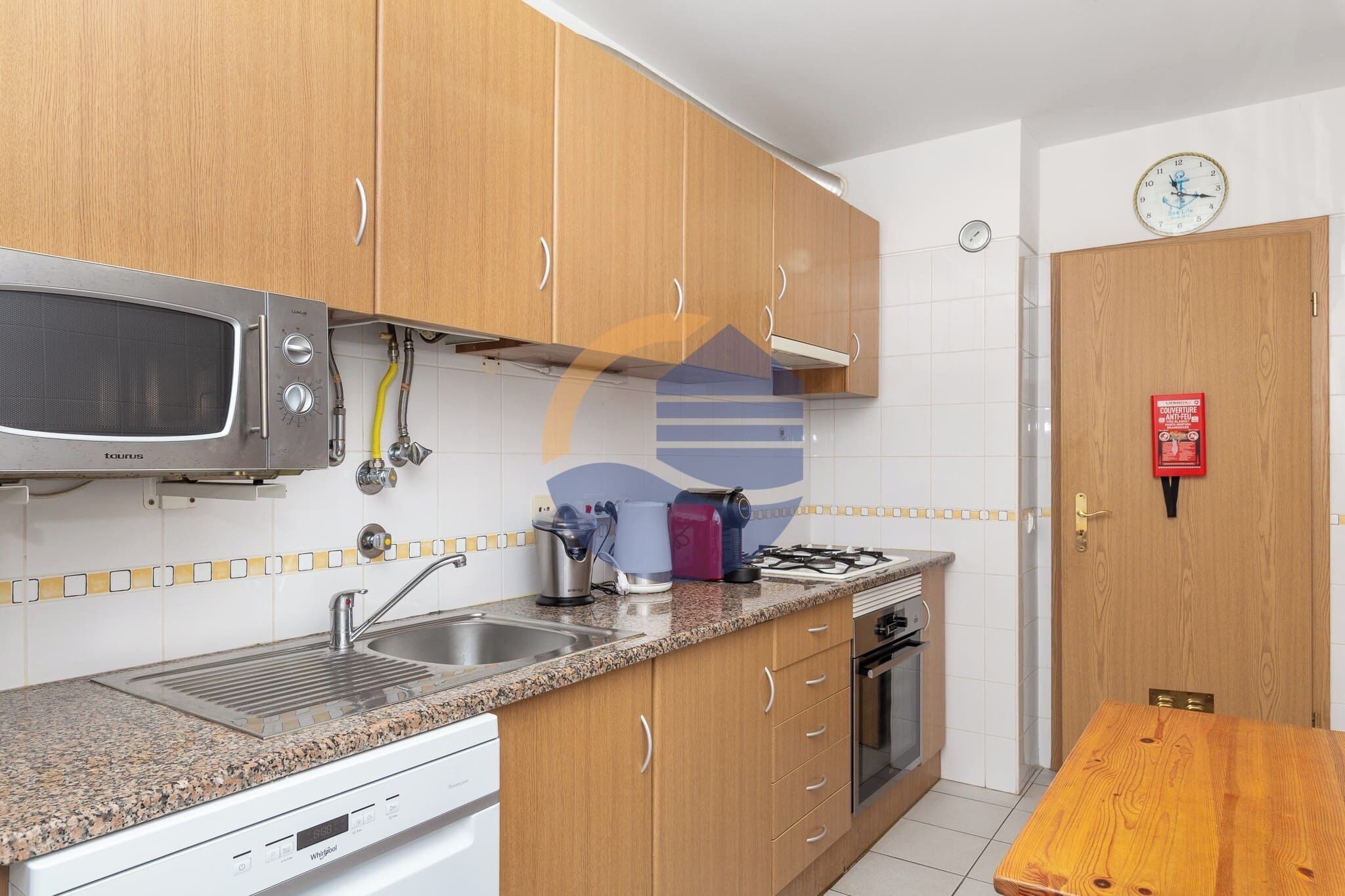 Una cocina con armarios de madera, un microondas de acero inoxidable, una estufa a gas y un fregadero.