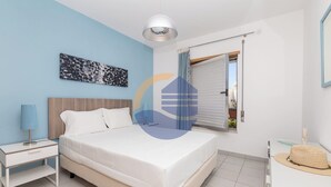 Ein Schlafzimmer mit einem Bett, einem Nachttisch, einer Lampe, einem Fenster mit Vorhängen und einem Wandbild.