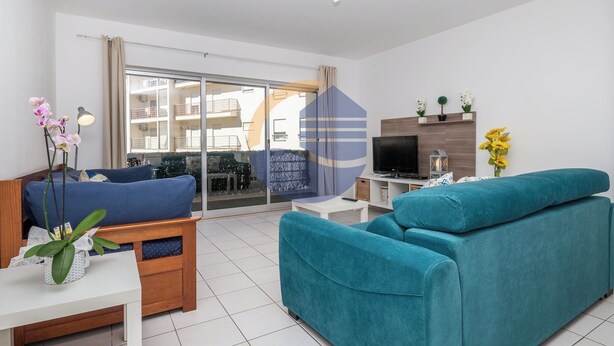 Ein modernes Wohnzimmer mit Sofa, Fernseher und einem Balkon mit Blick auf andere Gebäude.