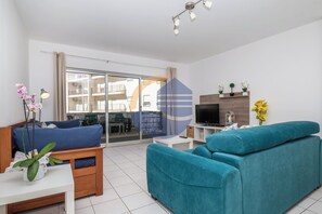 En moderne stue med sofa, fjernsyn og balkon med udsigt til andre bygninger.