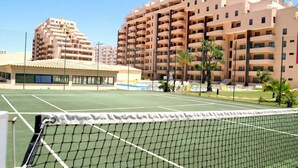 A tennis court with a net in the foreground, surrounded by multi-story residential buildings. - 3 Bedroom apartment Paraiso Sol da Rocha (Portimão)