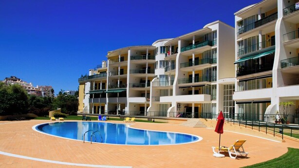 A modern hotel with a swimming pool, multiple balconies, and a well-maintained lawn. - 2 Bedroom apartment Condominio Primavera (Portimão)