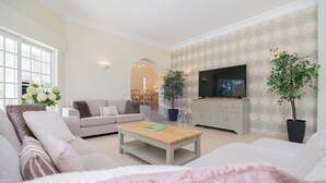 Ein Wohnzimmer mit einer Couch, einem Couchtisch, einem Fernseher und Topfpflanzen.