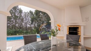 Ein Glastisch mit Korbstühlen, ein Kamin und Blick auf einen Pool und Bäume.