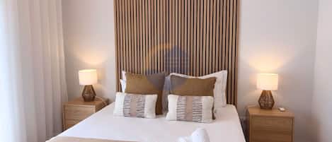 A neatly made bed with two pillows, a bedside table with a lamp, and a wall with vertical wooden slats.