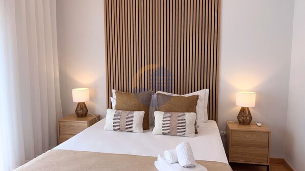 A neatly made bed with two pillows, a bedside table with a lamp, and a wall with vertical wooden slats.