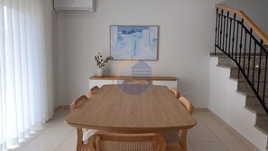 Un coin repas avec une table et des chaises en bois, un tableau au mur, une plante en pot et un escalier.