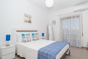 Ein Schlafzimmer mit einem Bett, Nachttischen, einer Lampe, einer blauen Decke und einem Fenster mit Vorhängen.