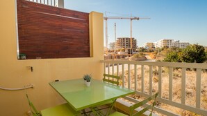 A balcony with a green table and chairs, a wooden fence, and construction cranes in the background.