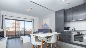 A modern kitchen with a dining area, large windows, and a view of a building. - One bedroom Duplex Paraíso Sol da Rocha (Portimão)