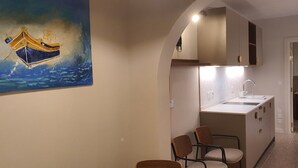 A compact kitchen with a white countertop, a sink, and a chair. There is a painting of a boat on the wall. - Capital Central Suites No2 - Peppa (Valletta, Malta,)