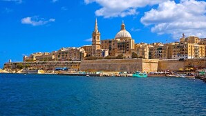 A coastal cityscape with historic buildings, a prominent church with a dome, and a fortified wall along the waterfront. - Capital Central Suites No2 - Peppa (Valletta, Malta,)