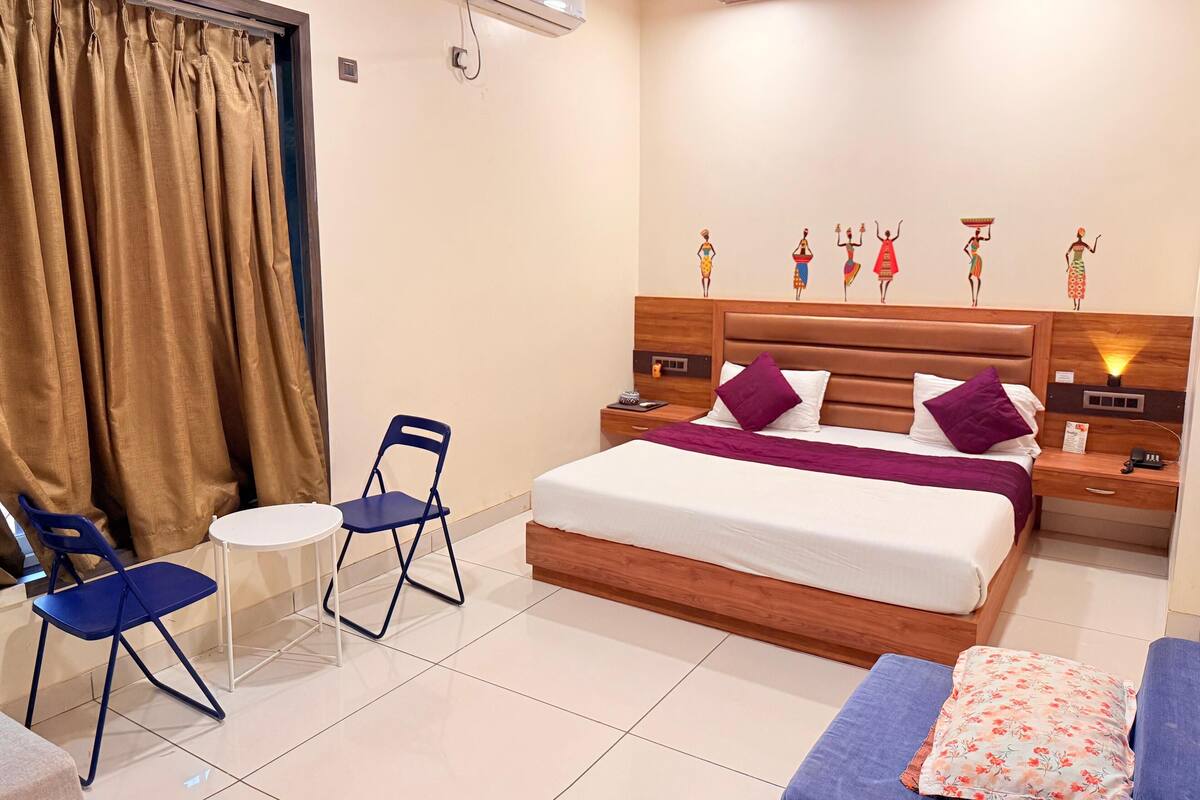 A hotel room with a bed, a chair, a small table, and a window with curtains.