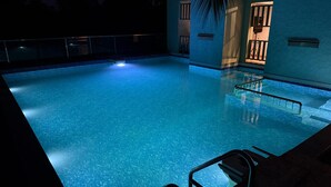 Piscina interior con agua cristalina, rodeada por un muro bajo y una palmera.