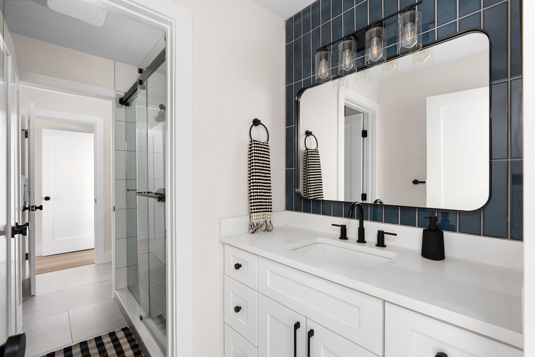 A modern bathroom with a white vanity, a large mirror, and a glass shower enclosure.
