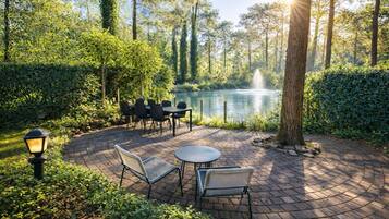 Une terrasse extérieure avec des tables et des chaises, un lampadaire et un bassin orné d’une fontaine.