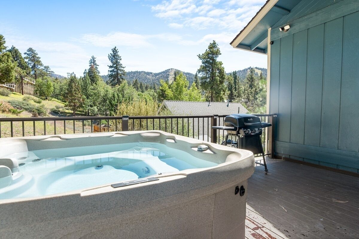 A hot tub on a wooden deck with a view of mountains and trees.