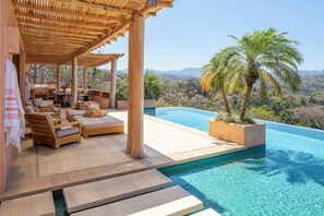 A poolside area with wooden loungers, a pergola, and a view of a mountain range. - Casa Naga Sayulita (Sayulita)