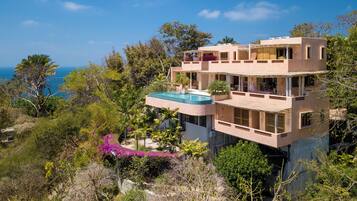 Una casa de varios pisos con piscina, rodeada de exuberante vegetación y vistas a un cuerpo de agua.