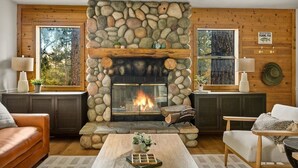 Una sala de estar acogedora con chimenea de piedra, paredes de madera y vistas al exterior.