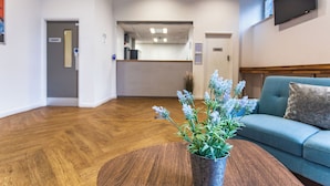 A reception area with a wooden floor, a blue sofa, a coffee table with a plant, and a TV mounted on the wall. - For Students Only Mealmarket Exchange in Aberdeen (Aberdeen)