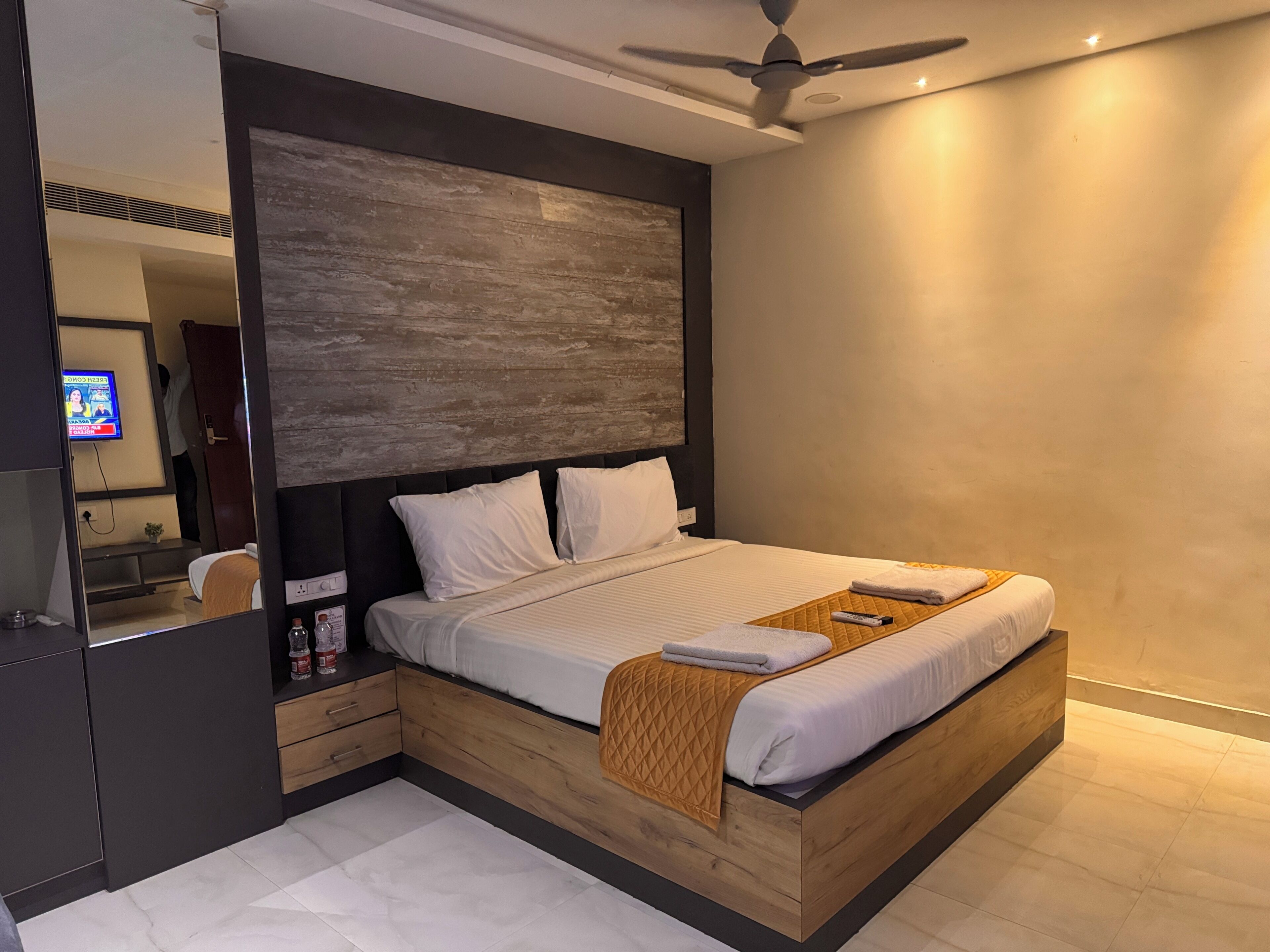 A modern bedroom with a wooden bed frame, a large mirror, and a ceiling fan.