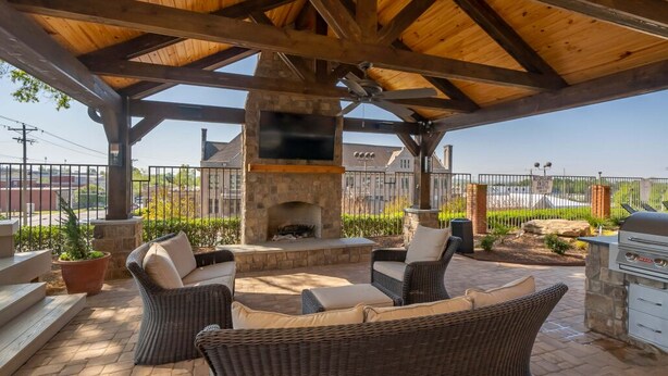 Une terrasse extérieure aménagée avec des meubles en osier, une cheminée en pierre et un barbecue.