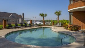 Une piscine avec des chaises longues, un indicateur de profondeur indiquant 3 pieds, et un bâtiment en briques doté d’un balcon.