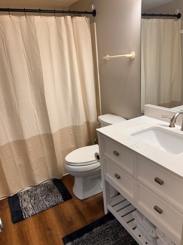 A bathroom with a toilet, a sink, a mirror, and a shower curtain.