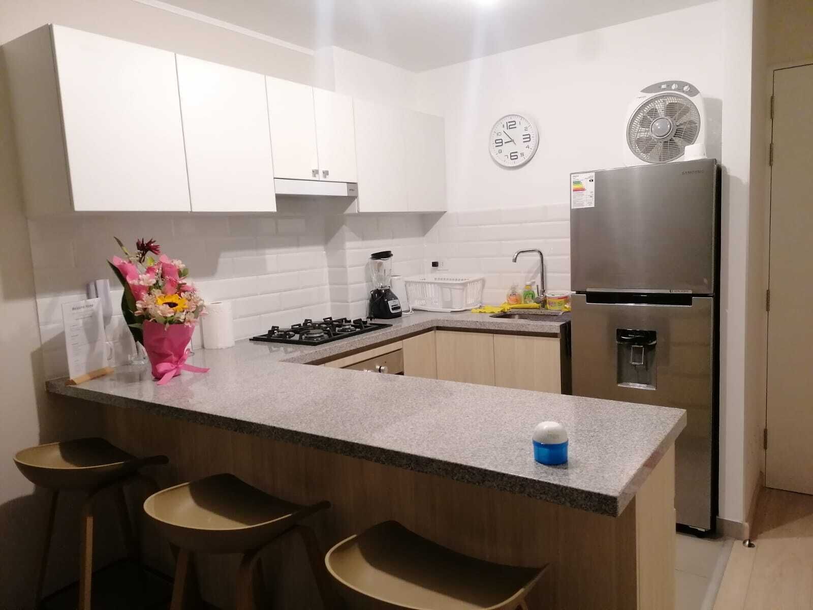 Eine moderne Küche mit weißen Schränken, einem Edelstahl-Kühlschrank, einem Gasherd, einer Spüle und einer Theke mit Barhocker.