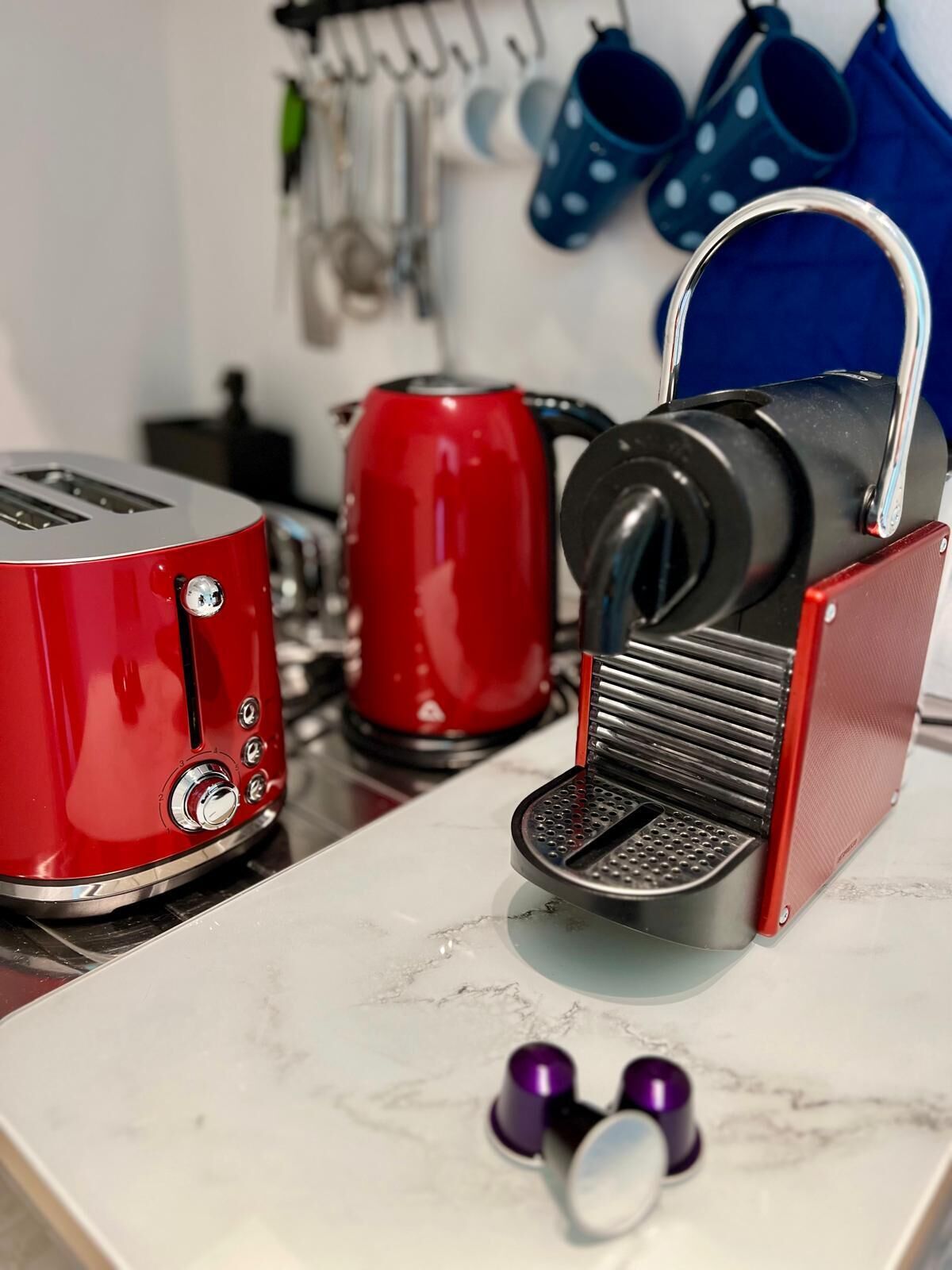 A kitchen with a red toaster, a red kettle, and a black coffee maker on a marble countertop.
