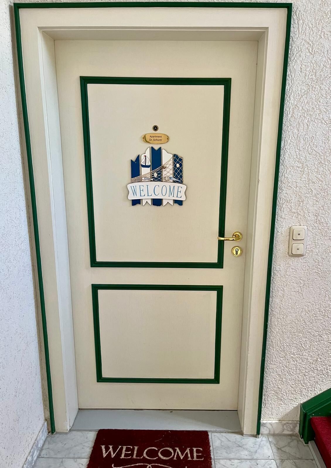 A door with a 'WELCOME' sign and a nameplate for 'Apartment Dr. Schuler'.