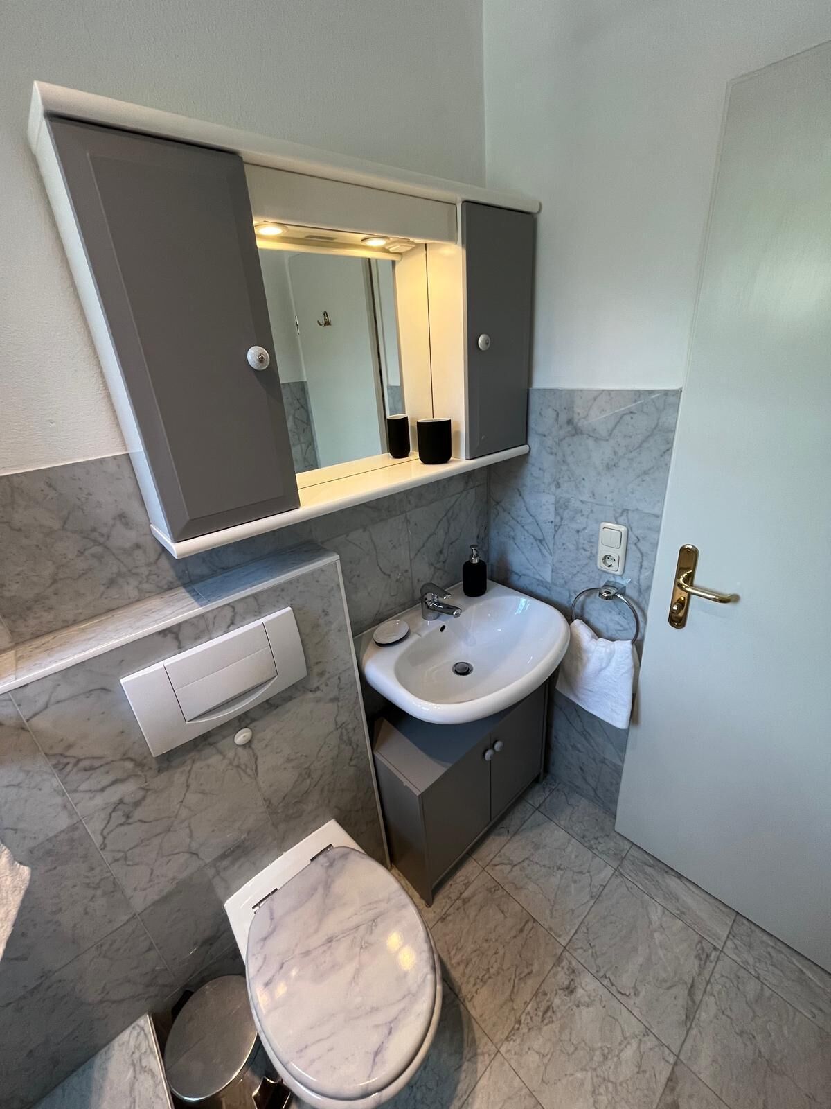 Un baño con lavamanos de mármol, inodoro y espejo sobre el lavamanos.
