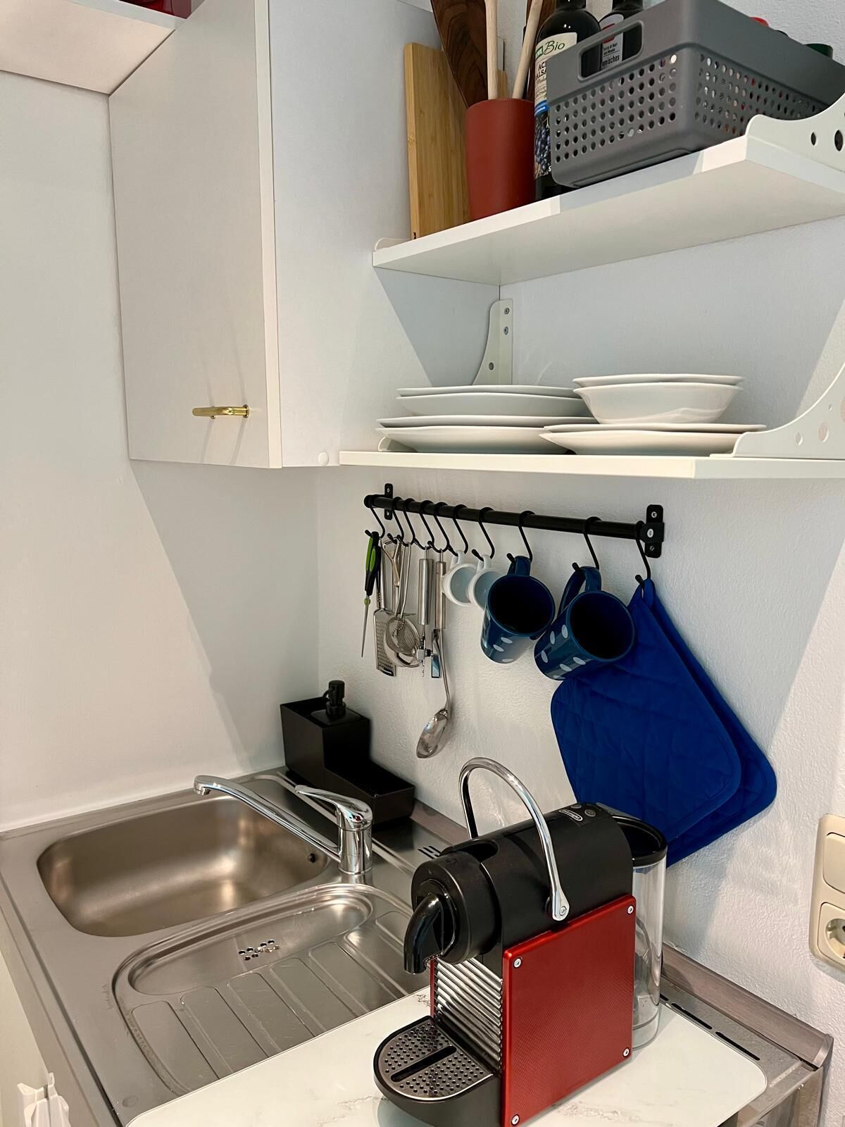 Una cocina con dos lavabos, una cafetera y utensilios colgados en un colgador.