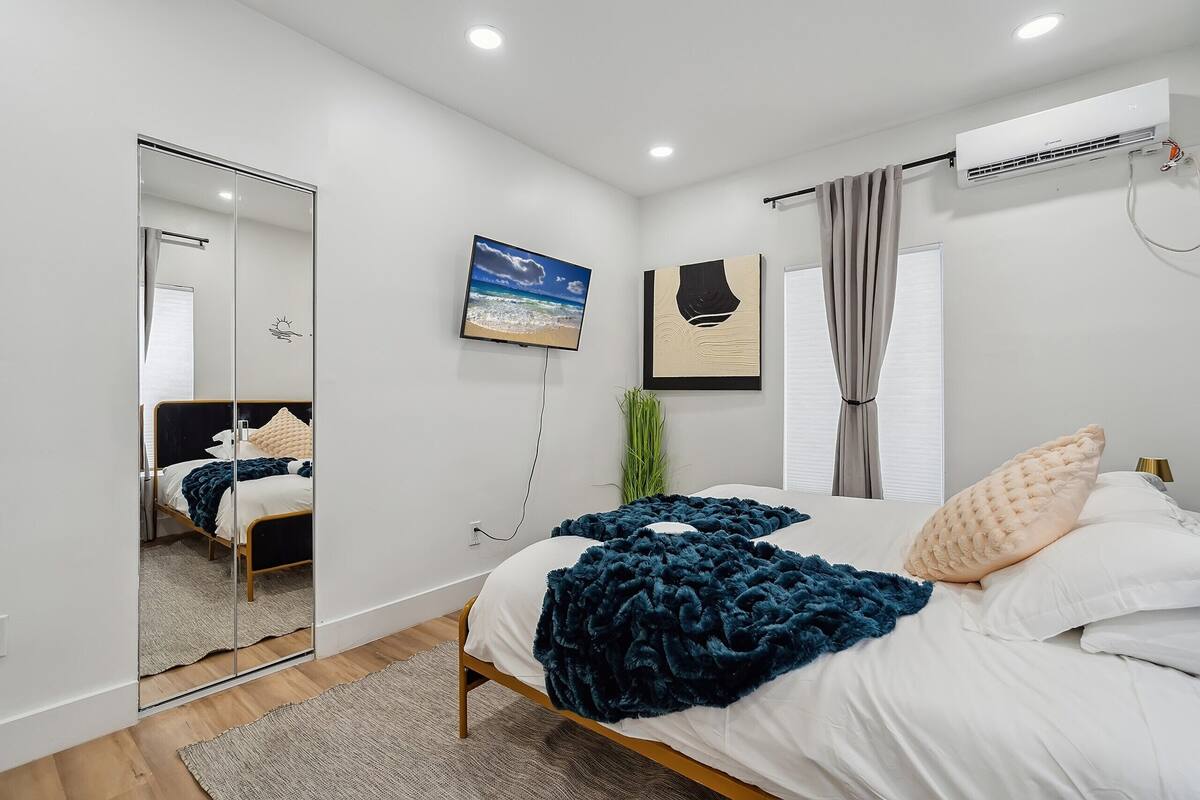 A modern bedroom with a large bed, a mirror, a TV, and an air conditioning unit.