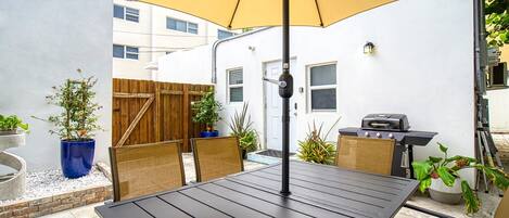 A patio with a table and chairs, a yellow umbrella, and a barbecue grill.